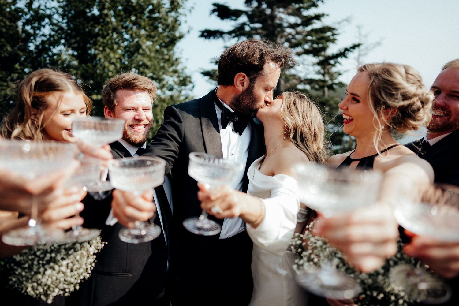 Wedding party celebrates with champagne toasts outdoors on a sunny day.