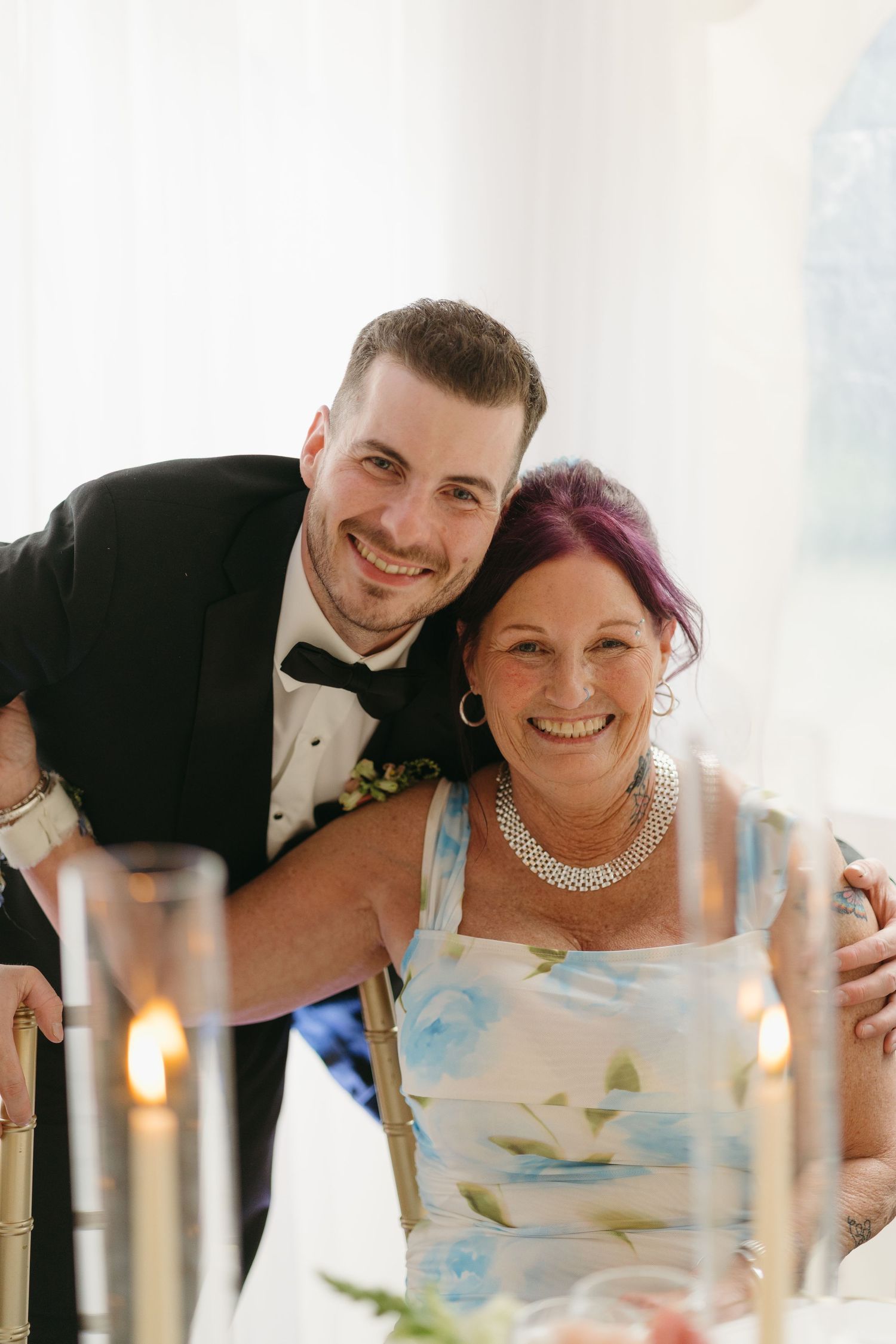 A couple shares a playful moment at their wedding reception table with lit candles.