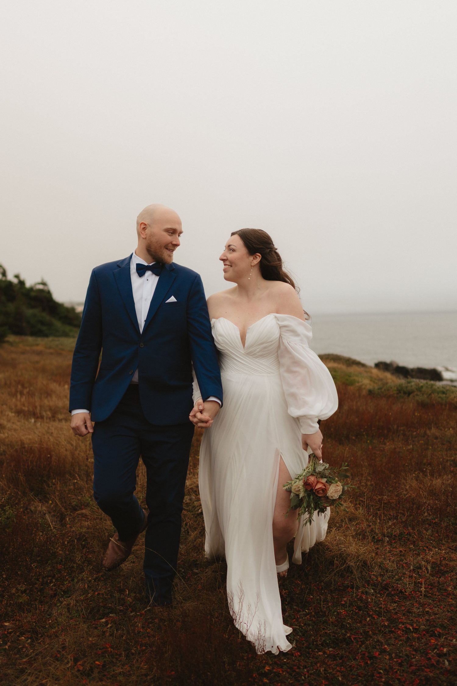 Newlywed couple walking together across a rustic hillside landscape during an intimate outdoor wedding ceremony.