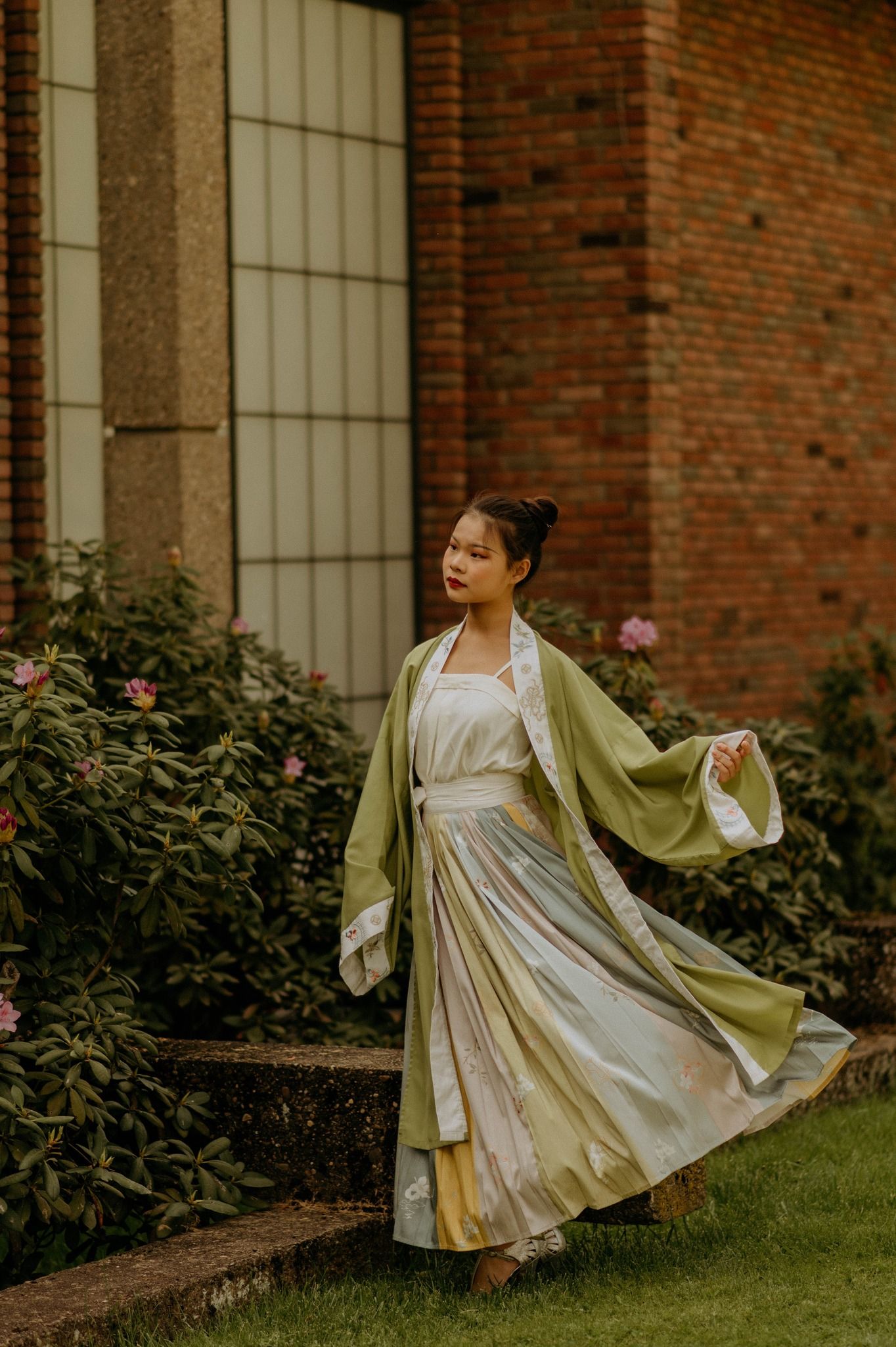 Person in hanfu dress with flowing robes spinning in a garden near a brick building in Pittsburgh PA, by Miranda Nicole Photo + Video.