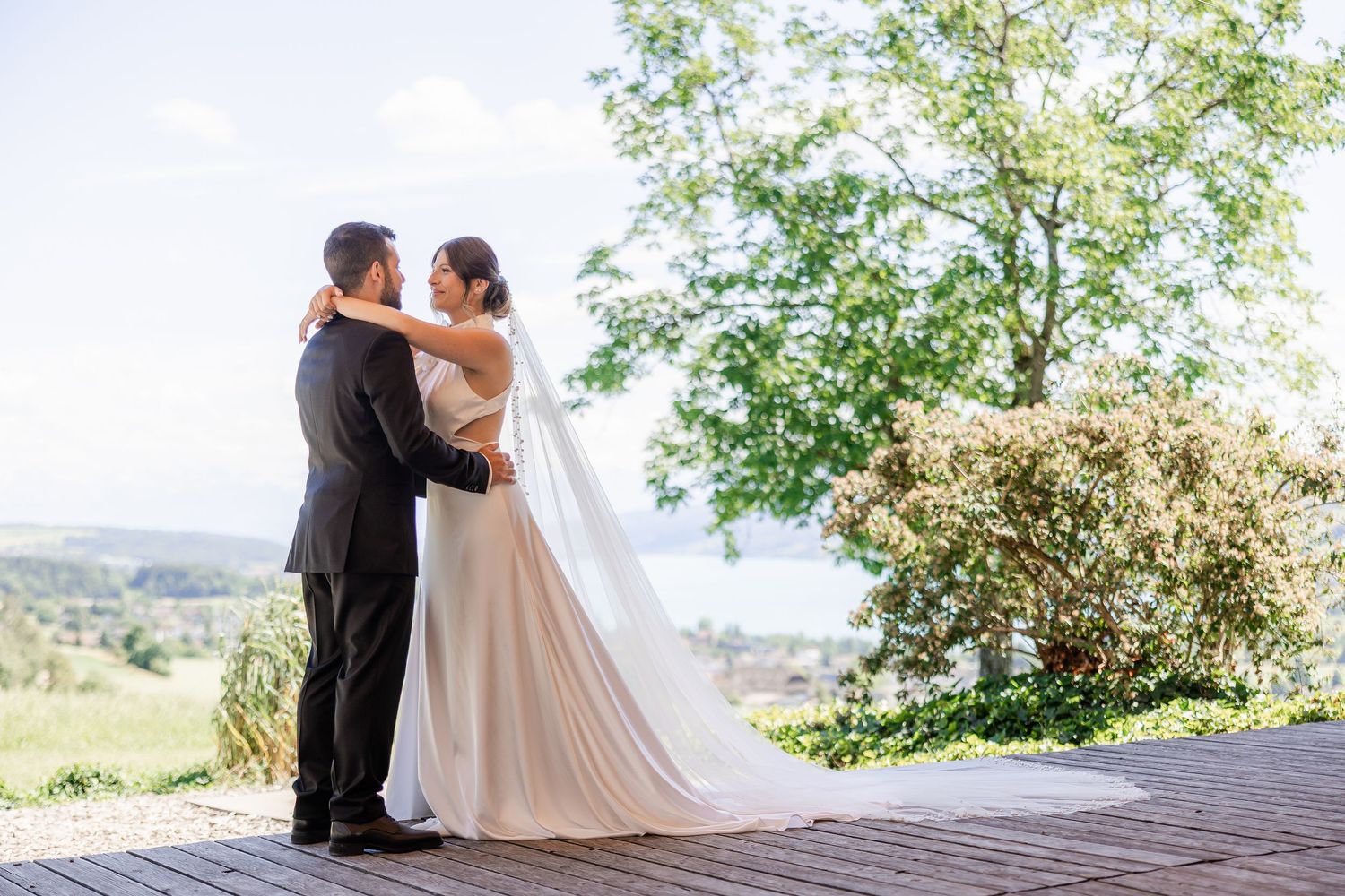 A bride and groom share a romantic embrace on a wooden terrace surrounded by lush greenery on their wedding day.