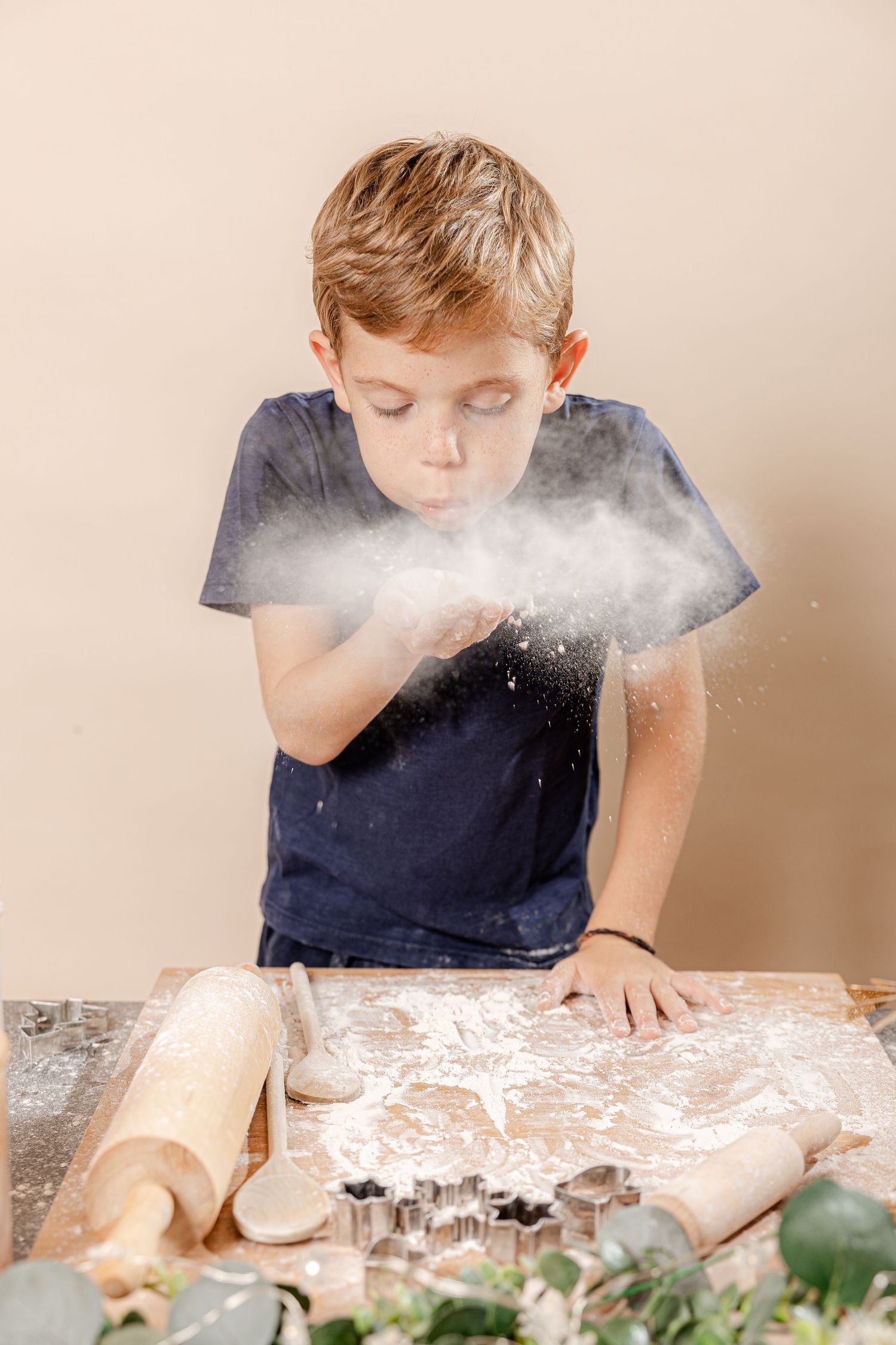 A sequence of photos shows flour being blown across a rustic table with greenery and cookie cutters.