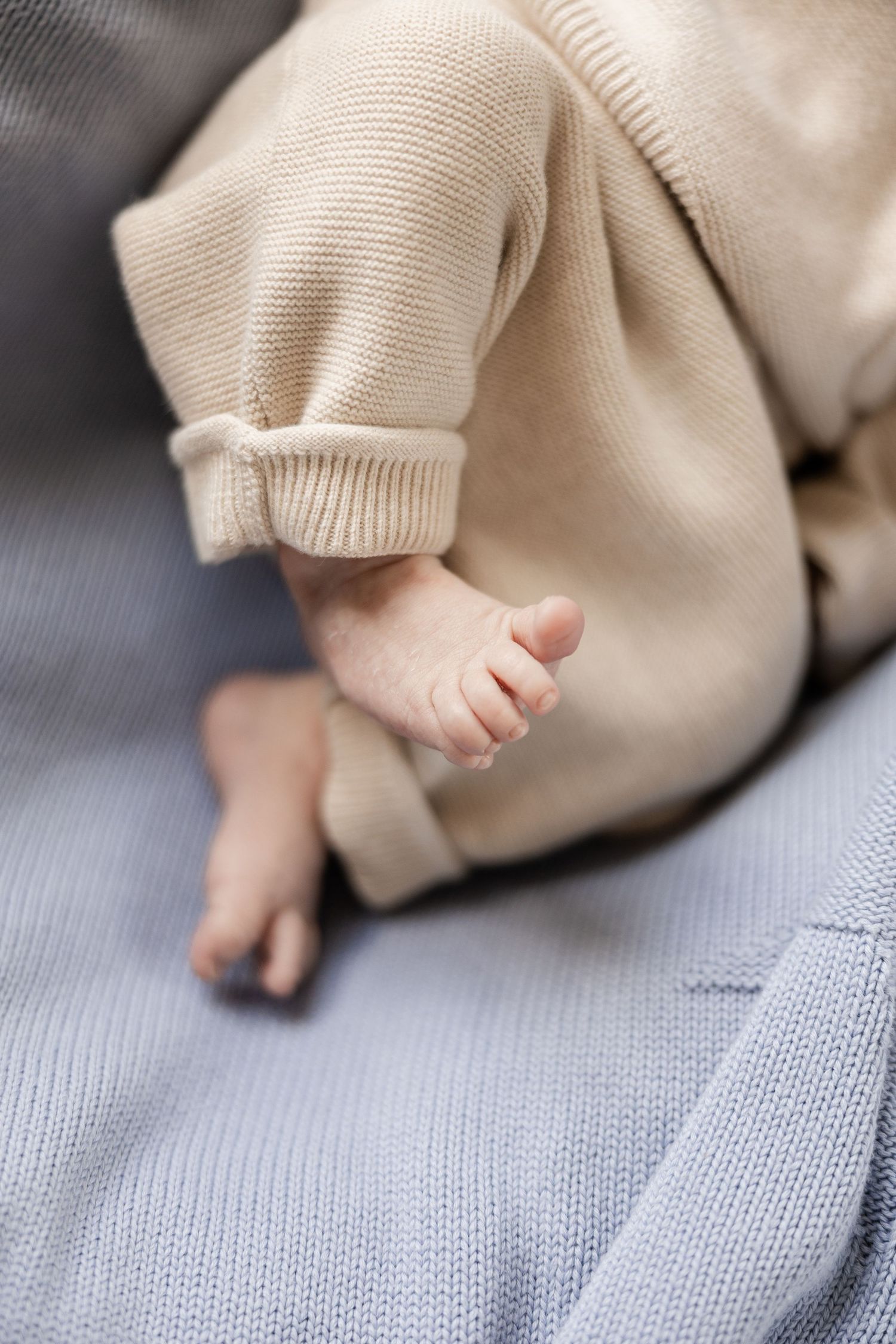 Close-up series of a baby's tiny toes peeking out from under a soft beige knit blanket on gray fabric. Baden, Aargau