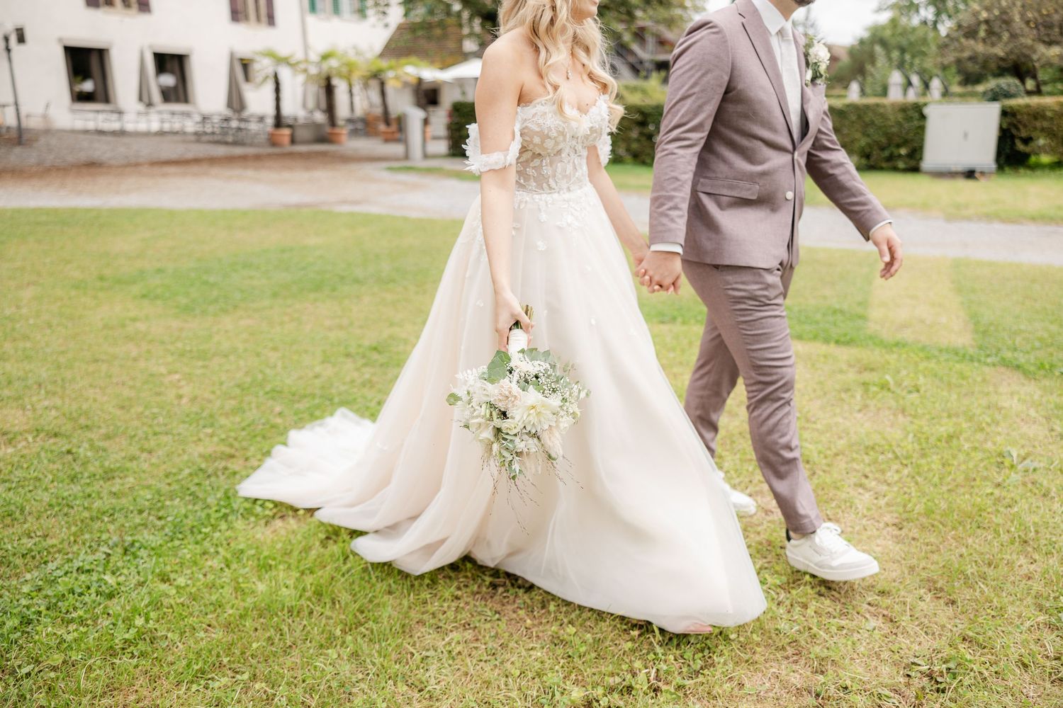 A bride and groom walk together across a manicured lawn at their outdoor wedding celebration.