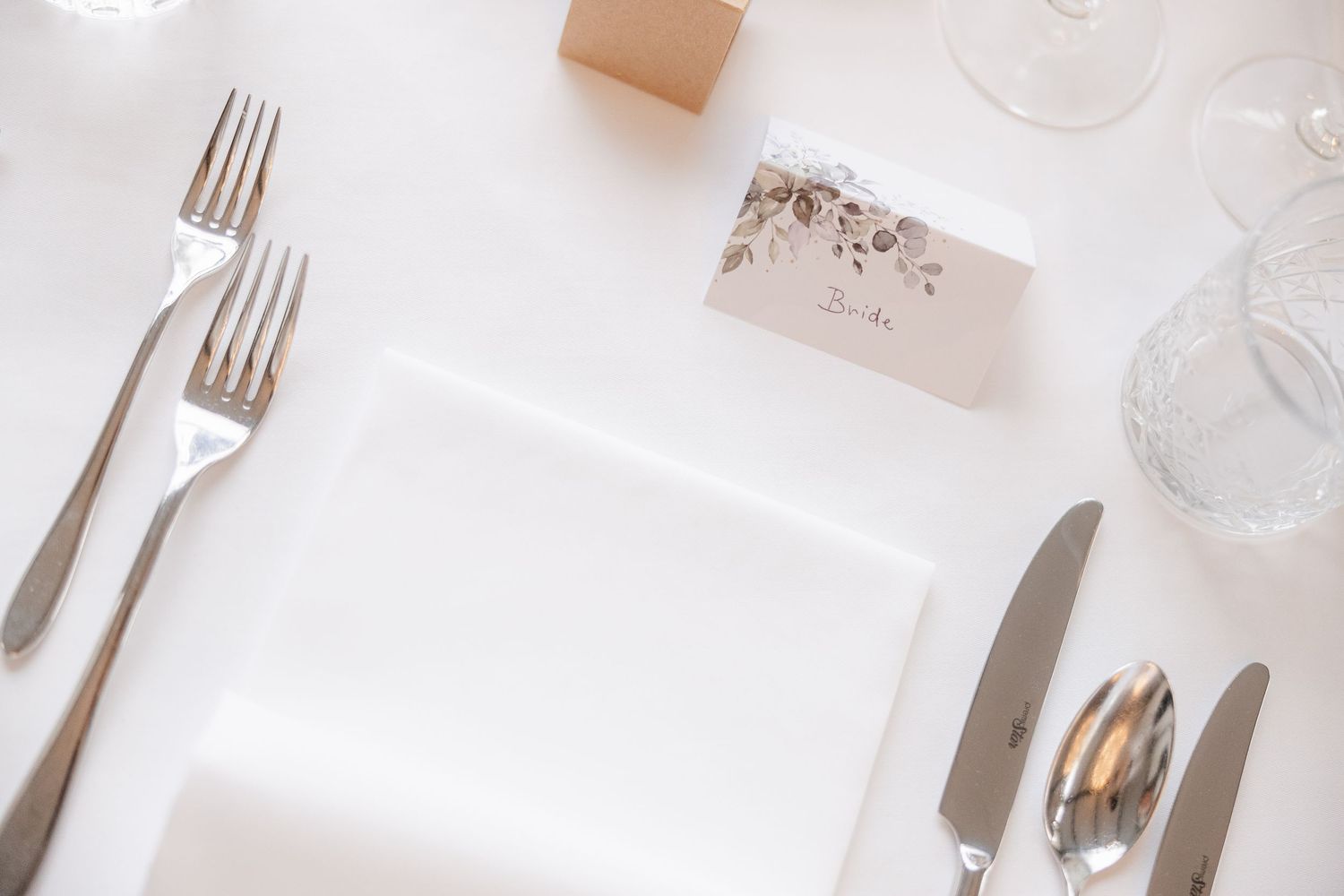 Elegant table setting with white plates, silverware, and crystal glasses arranged on a light colored surface.
