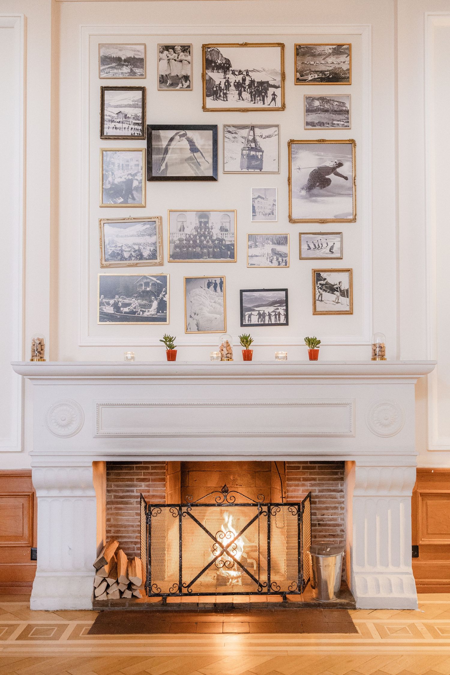 A white fireplace mantel decorated with vintage black and white framed photographs and small potted plants on the ledge.