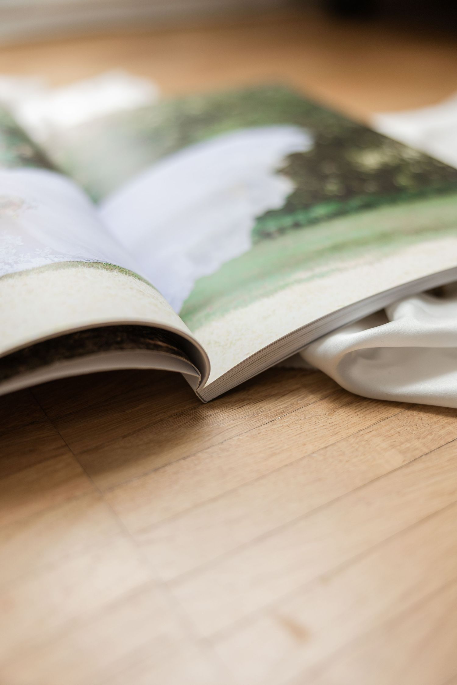 An open magazine with blurred pages lies on a wooden surface with soft focus and shallow depth of field.