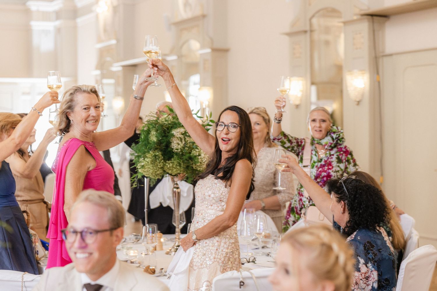 Wedding reception guests raise their glasses in celebration at an elegant venue with floral decor - Hochzeitsfotograf Schweiz