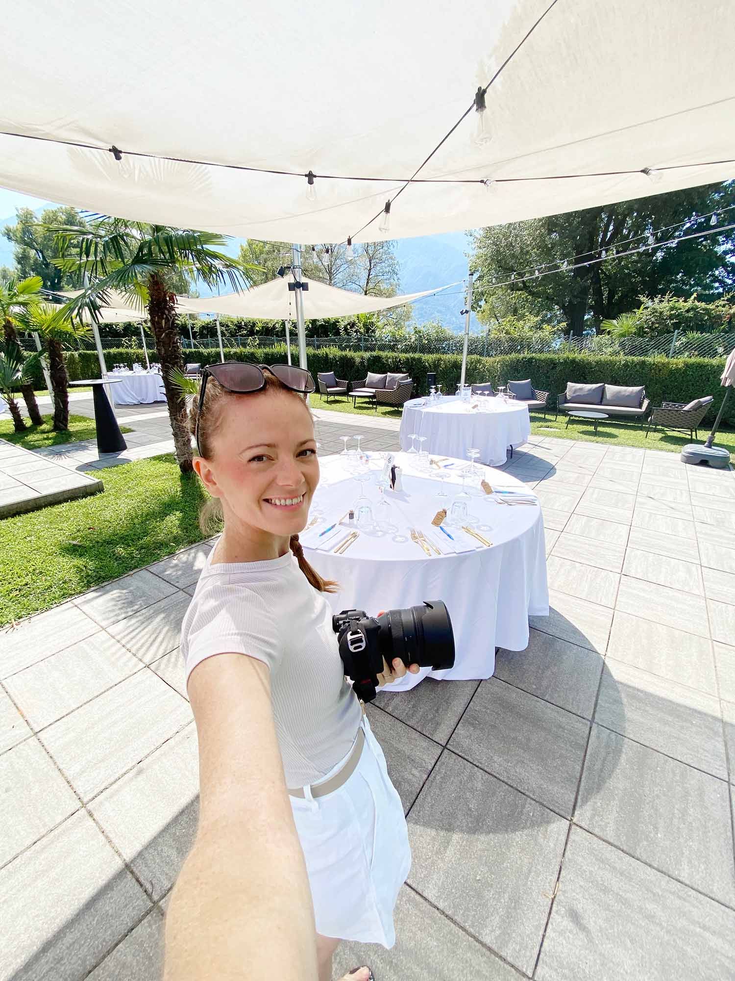 A sunny outdoor event space with white tablecloths and string lights decorating a modern patio area.