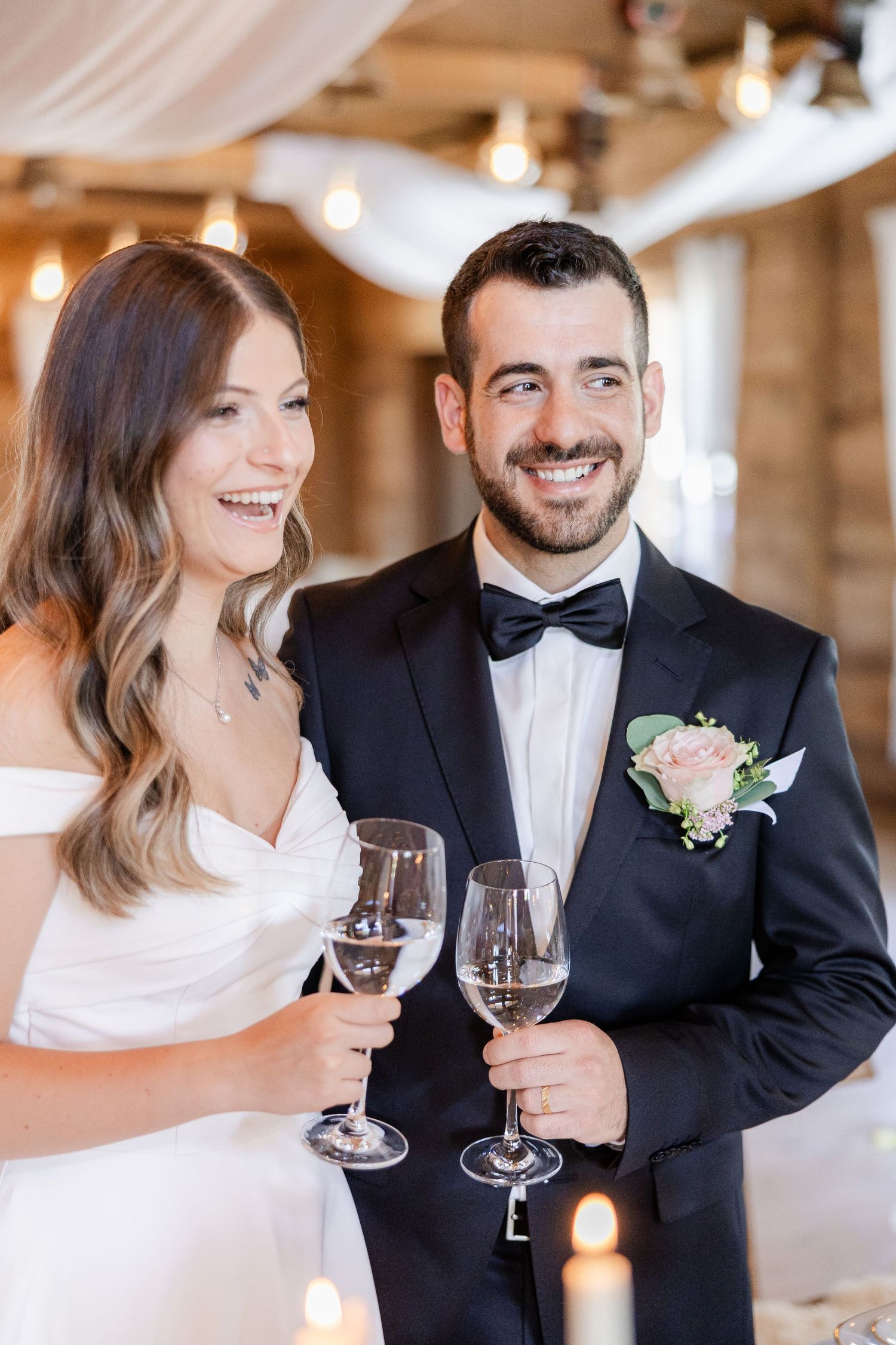 Smiling bride and groom in wedding attire toasting with champagne glasses at their elegant reception venue.
