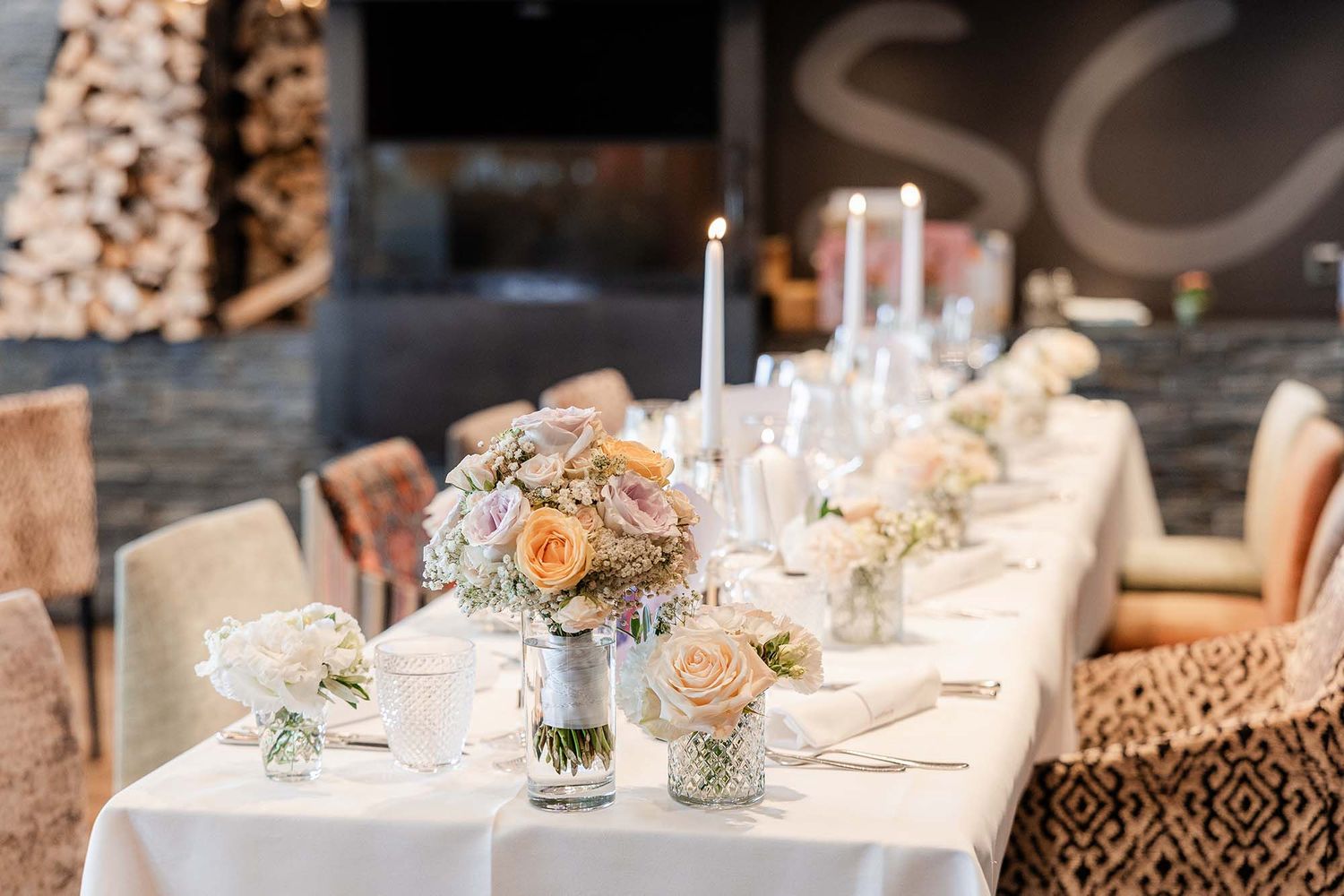 Elegant wedding reception table set with white linens, candles, and pastel floral arrangements in a sophisticated venue.