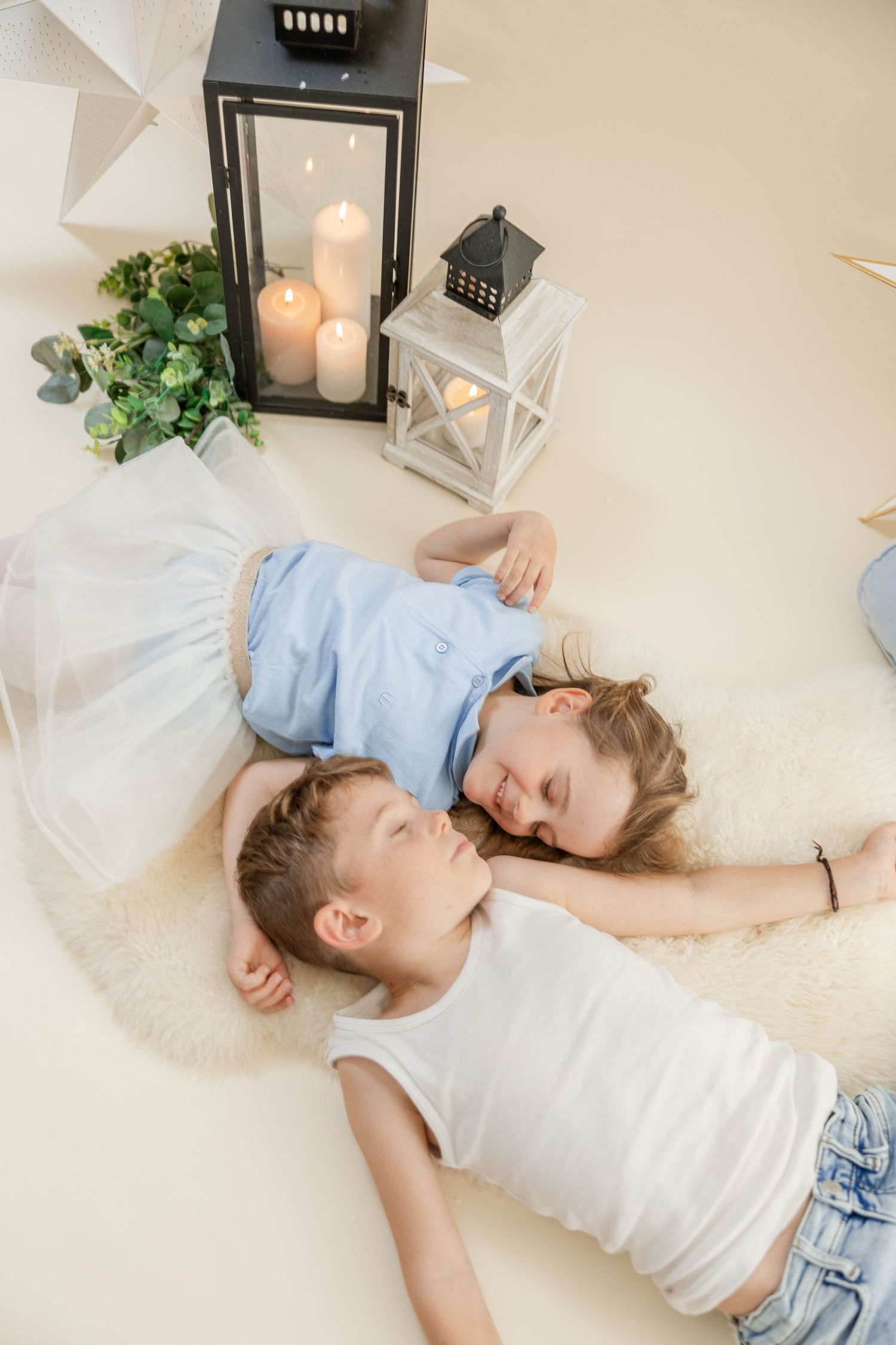 Two people lying on a white floor with lanterns and greenery decorations in a dreamy setting.