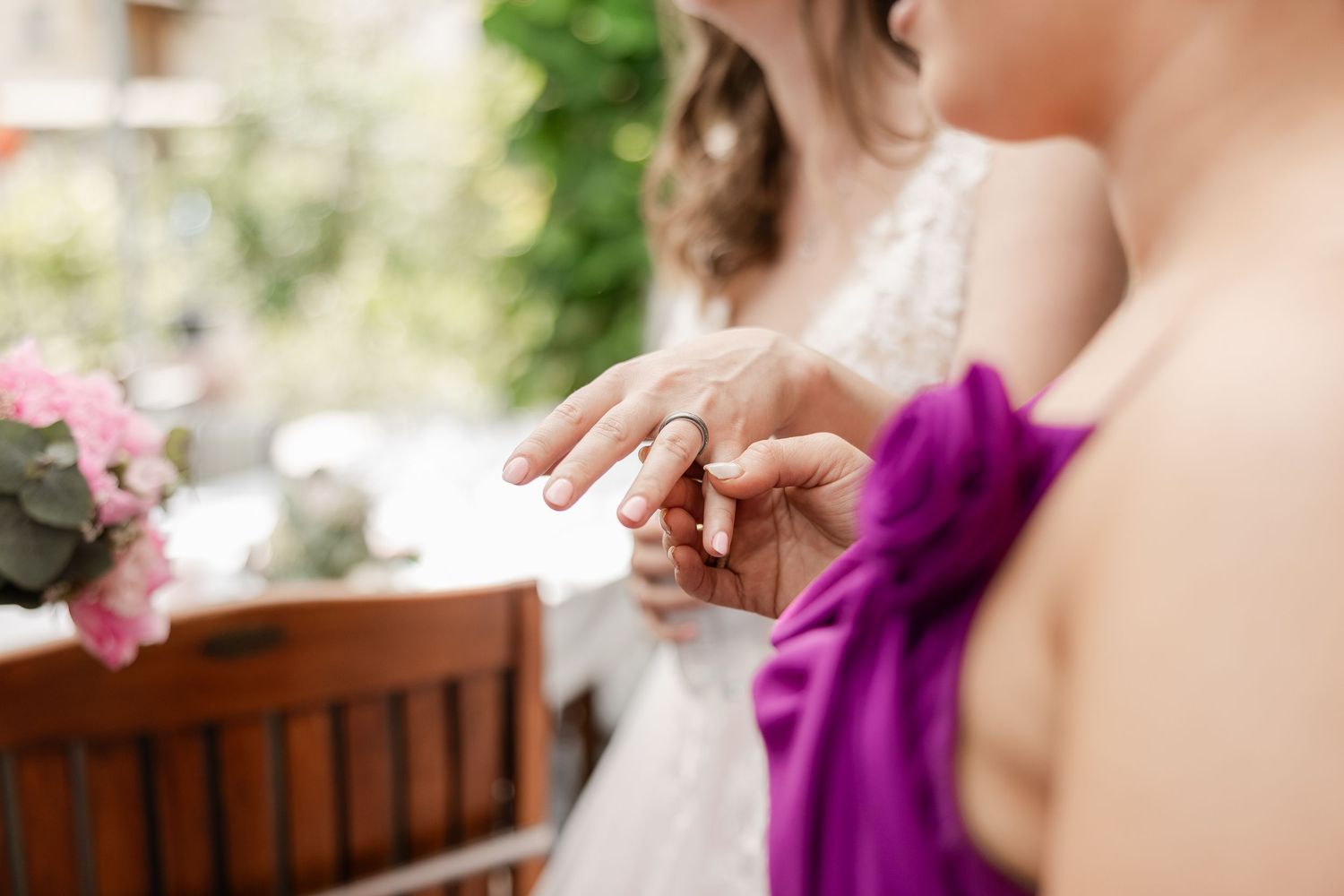 Bride shows her delicate wedding ring to a wedding guest in purple dress.