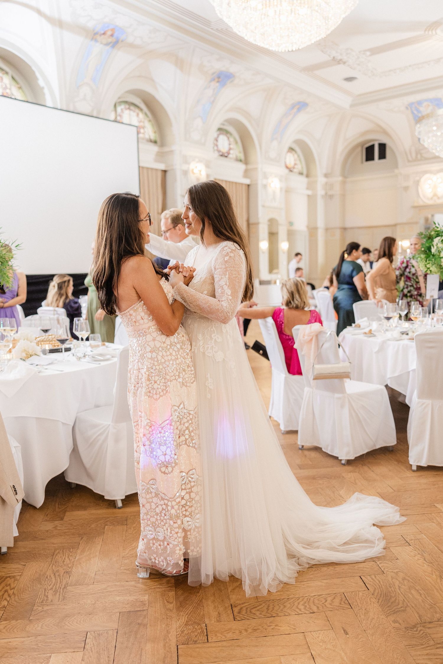 Wedding guests dance and celebrate in an elegant white ballroom with ornate details and round tables - Hochzeitsfotograf Schweiz