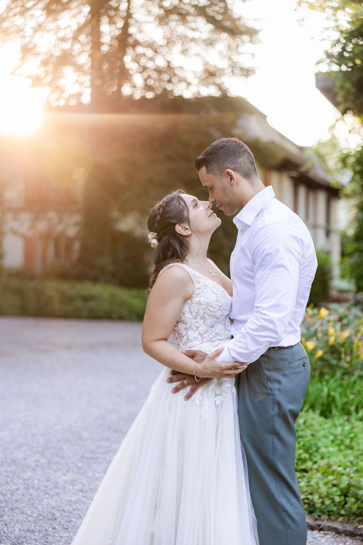 Bride and groom share a romantic moment at golden hour in a lush garden, with warm sunlight glowing behind them.