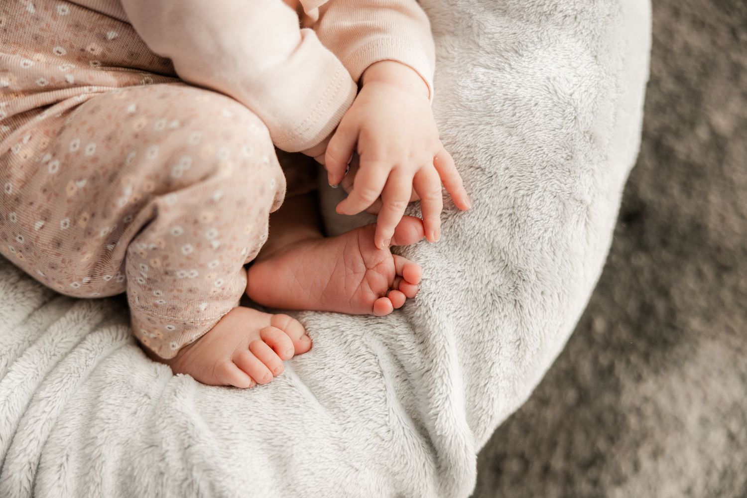 Close-up view of tiny baby feet and hands resting on soft textured gray blanket.