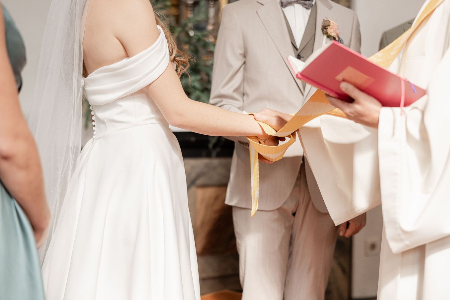 A couple exchanges rings during an outdoor wedding ceremony as an officiant holds a red book.