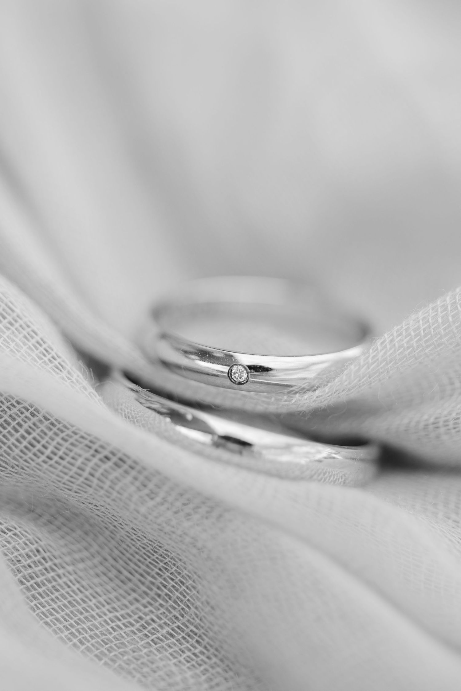 Close-up view of silver wedding rings resting on soft white fabric showing fine details and texture.