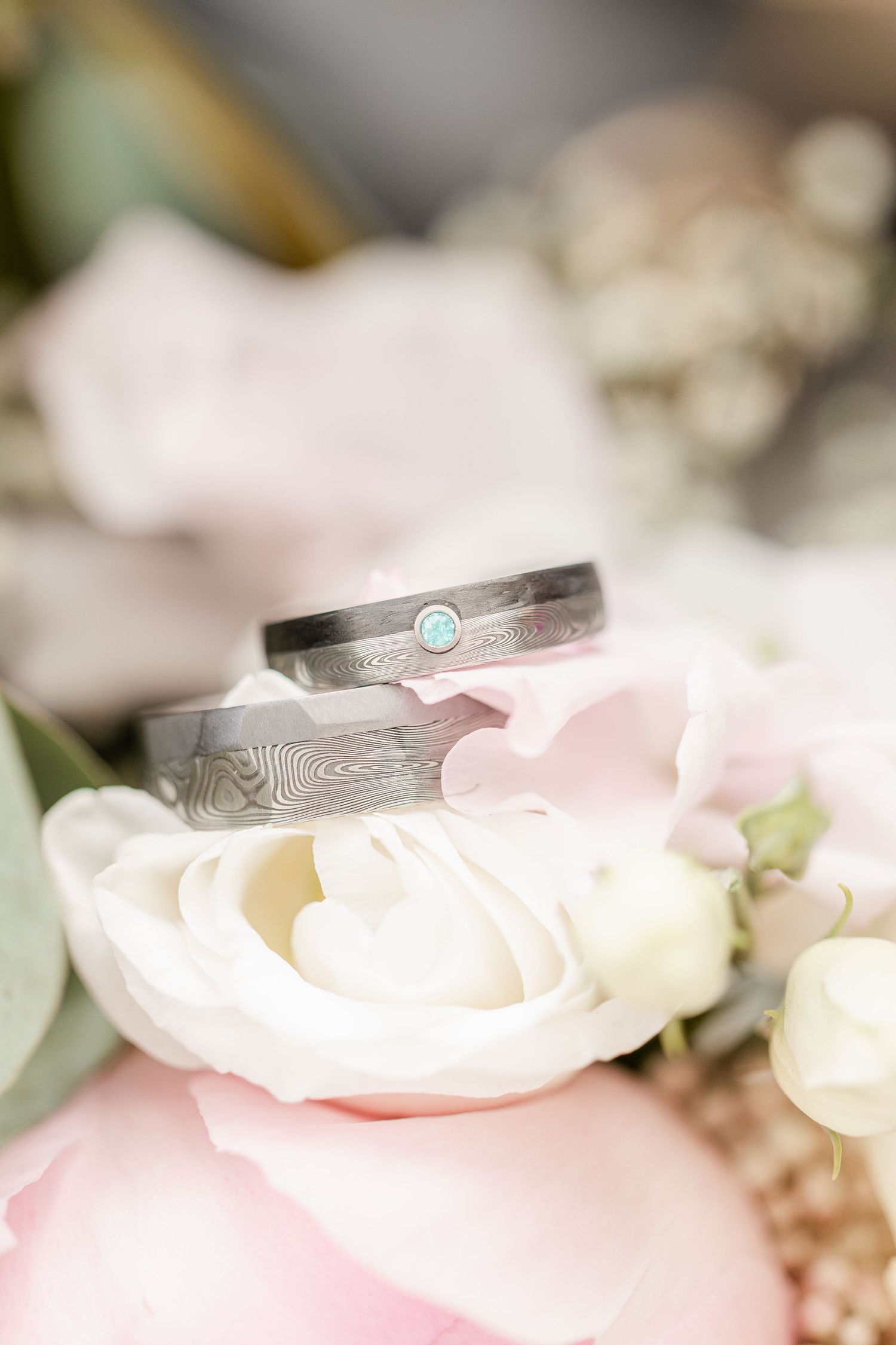Two textured wedding rings with a turquoise stone displayed on soft pink and white roses.