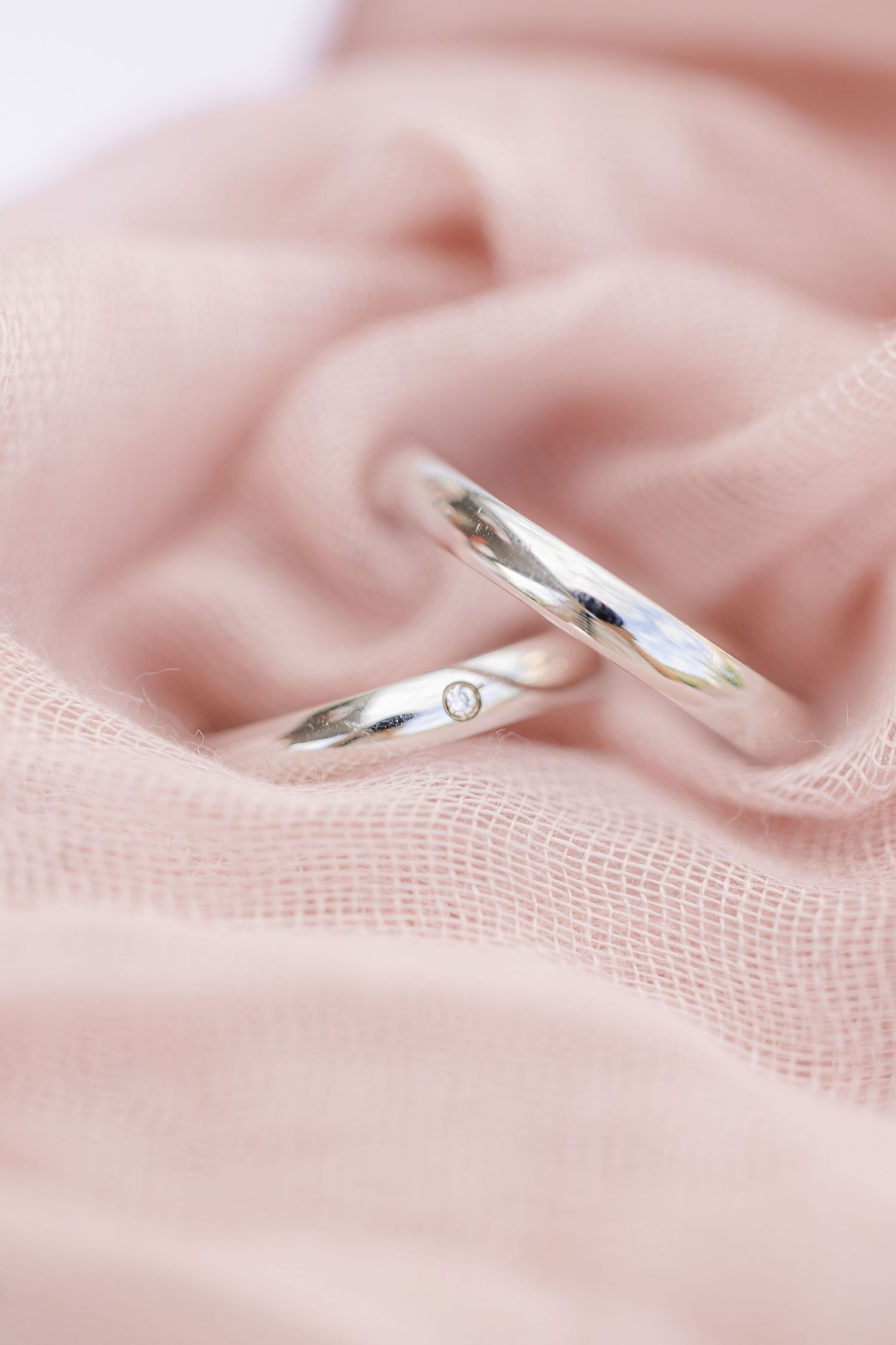 Two silver wedding rings rest on soft pink fabric with delicate texture and gentle folds.