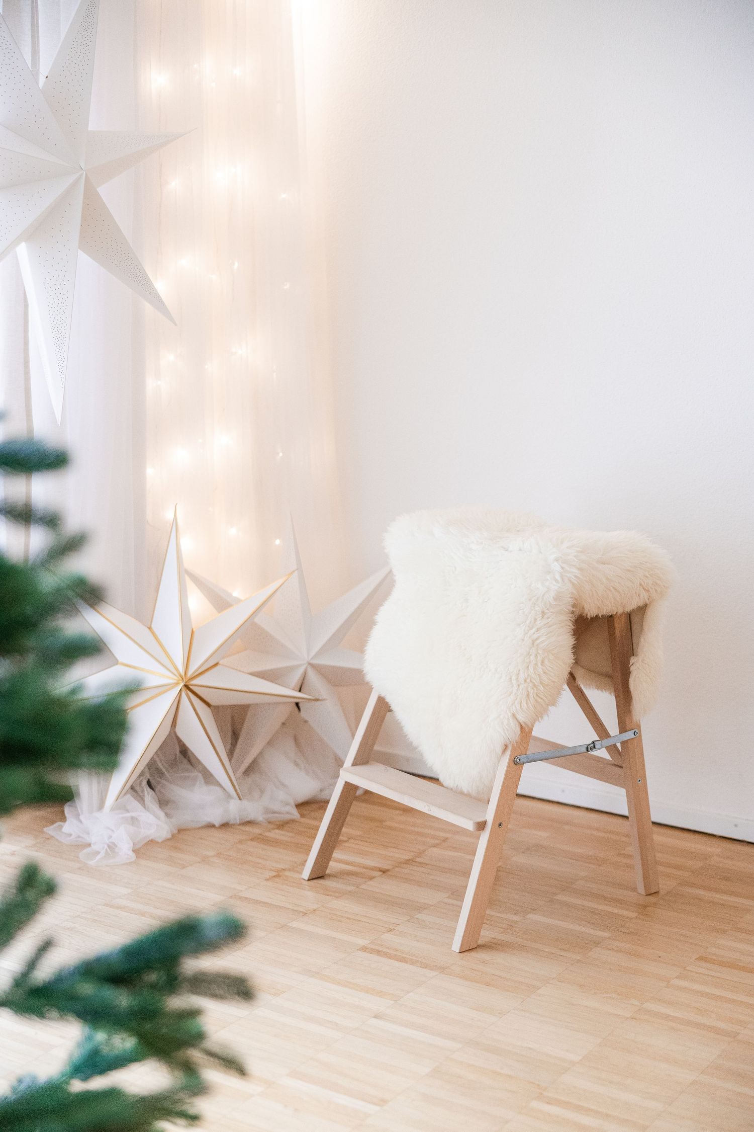 White origami paper star decorations hang from the ceiling over a wooden stool in a minimalist room setting.
