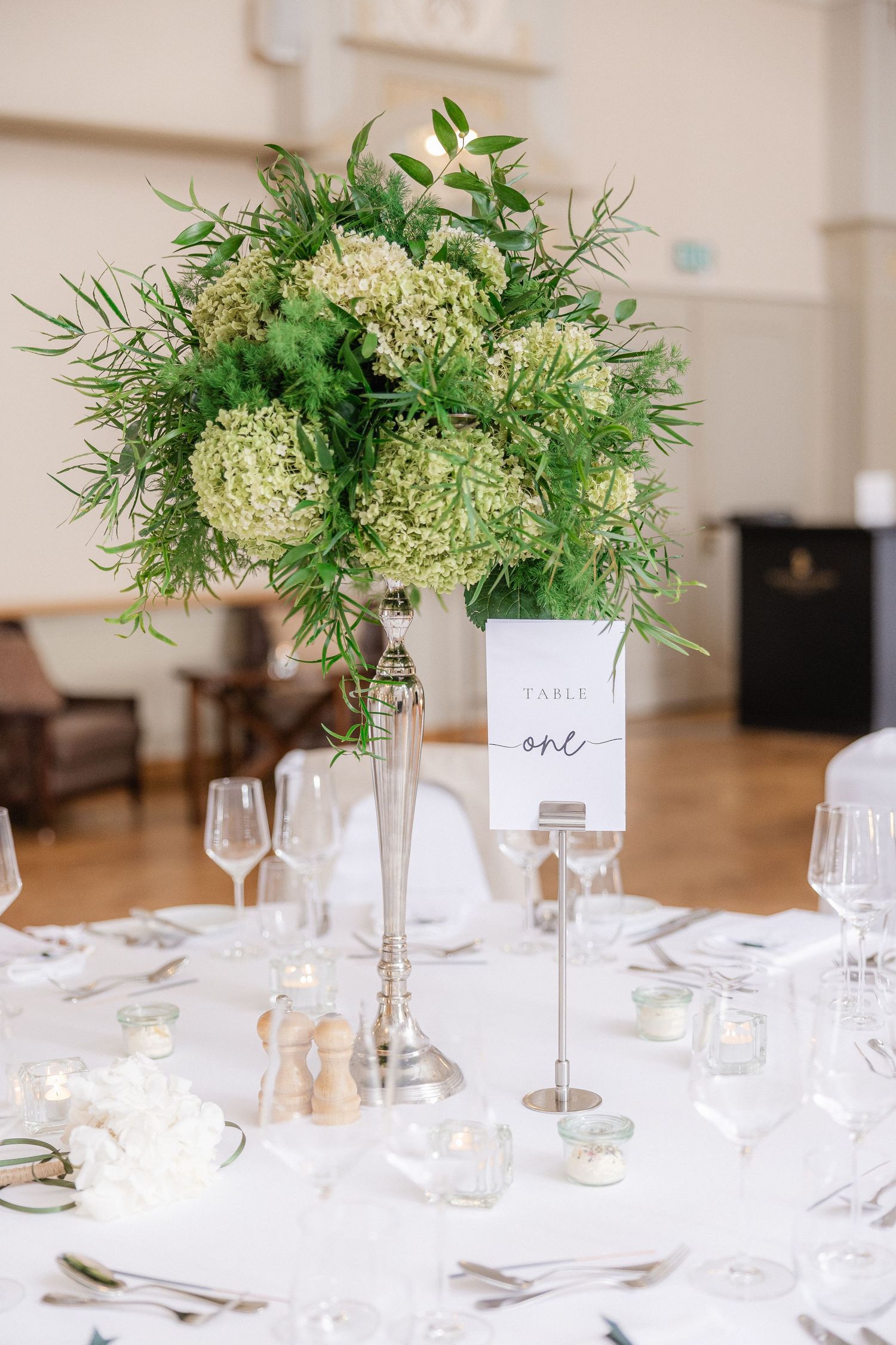 Elegant wedding table settings with tall glass vases holding white hydrangea and greenery centerpieces.