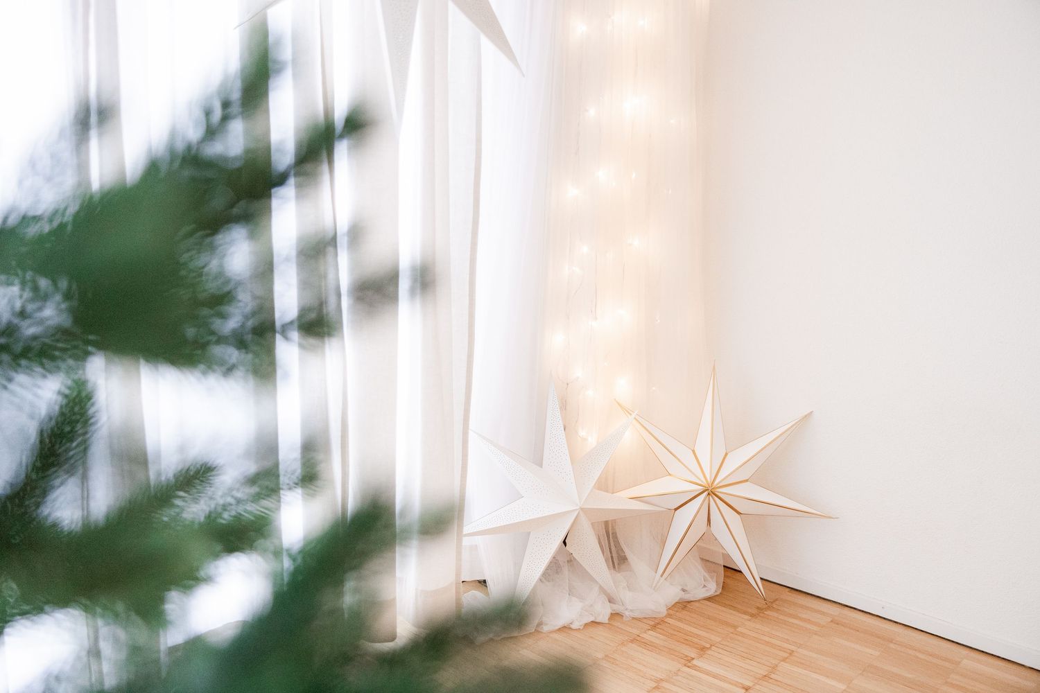 Decorative paper star lanterns hanging from strings against a white wall with green foliage visible in background.