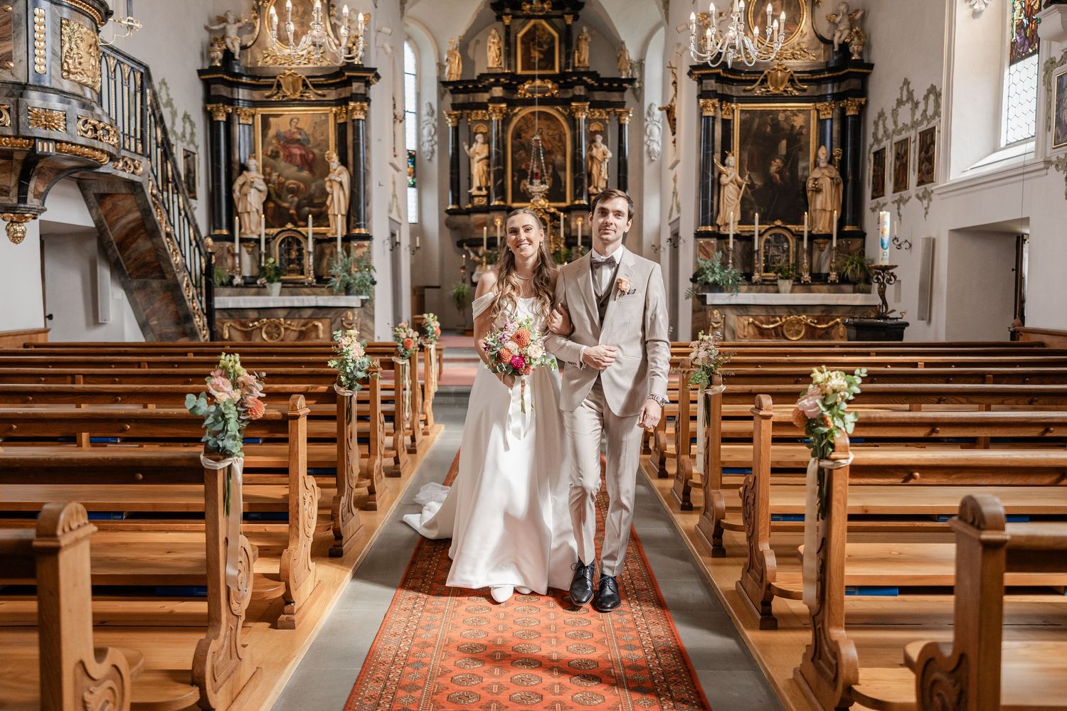 Interior of a traditional church with wooden pews and ornate altars illuminated by natural light.