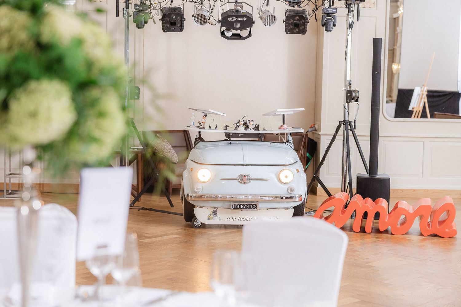 A modern white wedding venue space with stage lighting equipment and decorative floral arrangements.