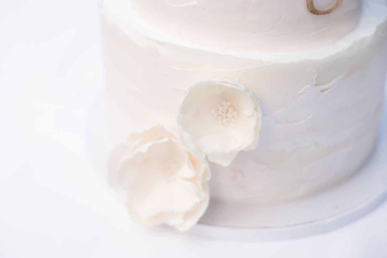 Elegant two-tier white wedding cake with delicate sugar peony flowers and textured buttercream frosting.