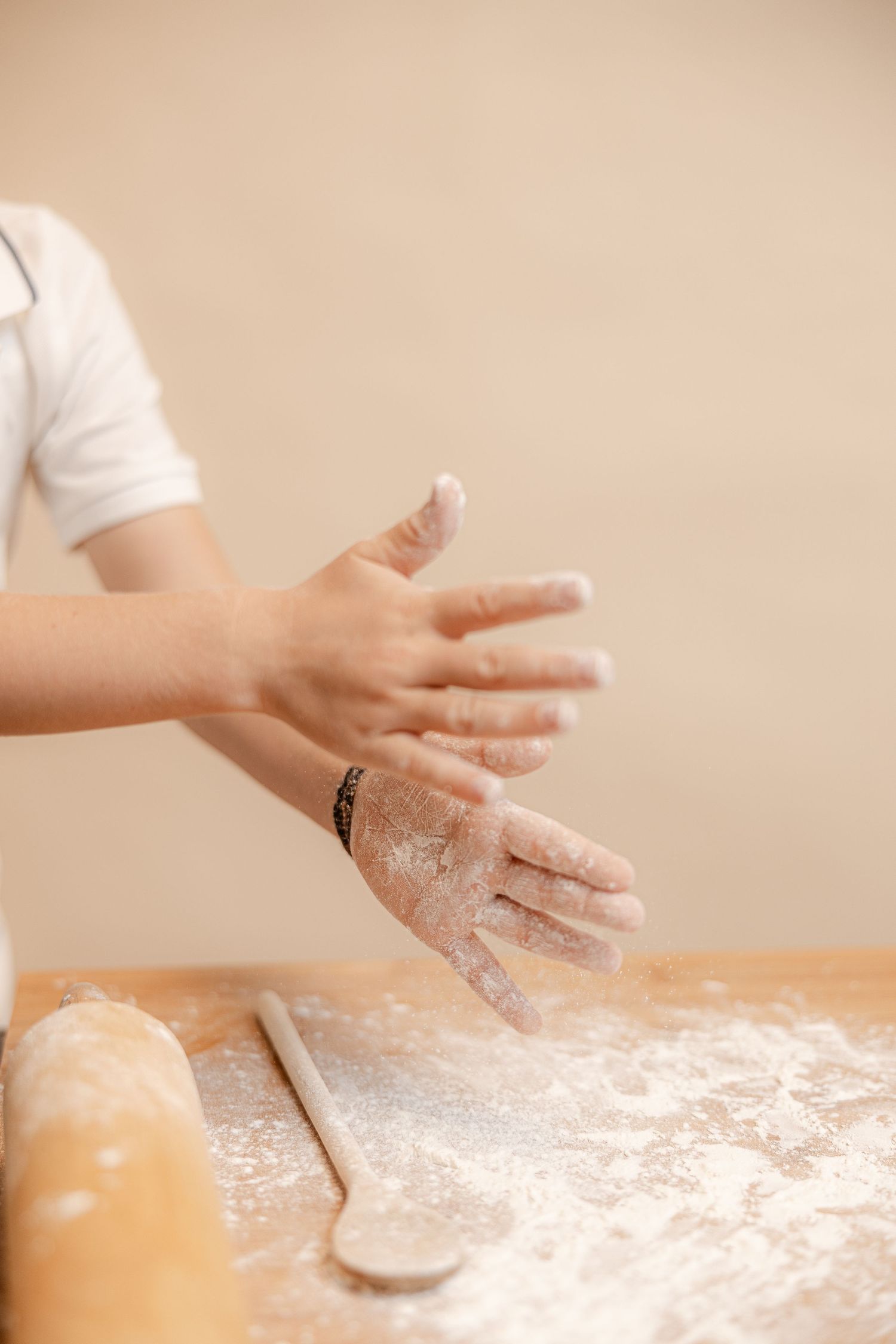 Hands dusted with flour working on a wooden surface with rolling pin and dough for baking preparation.