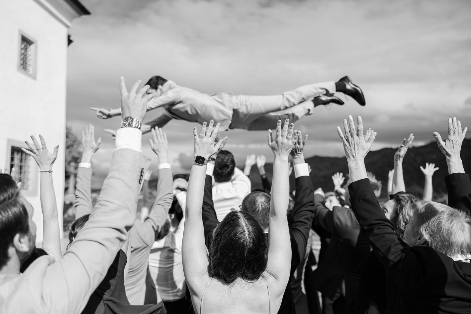 Black and white photo of wedding guests raising their hands and dancing during a lively reception celebration.