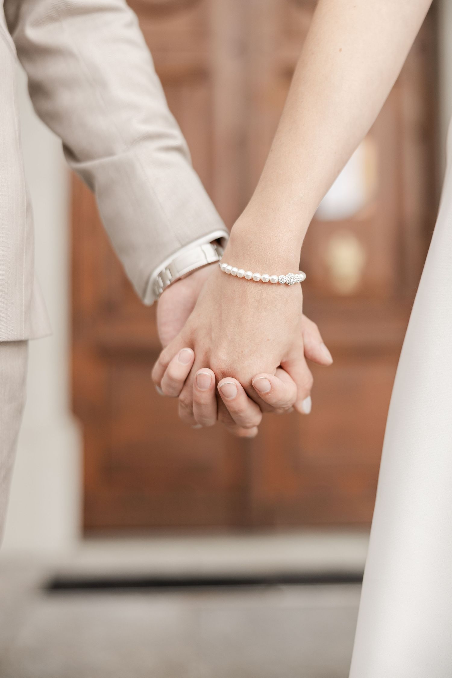 Close-up view of hands wearing a pearl bracelet holding each other in an intimate moment.