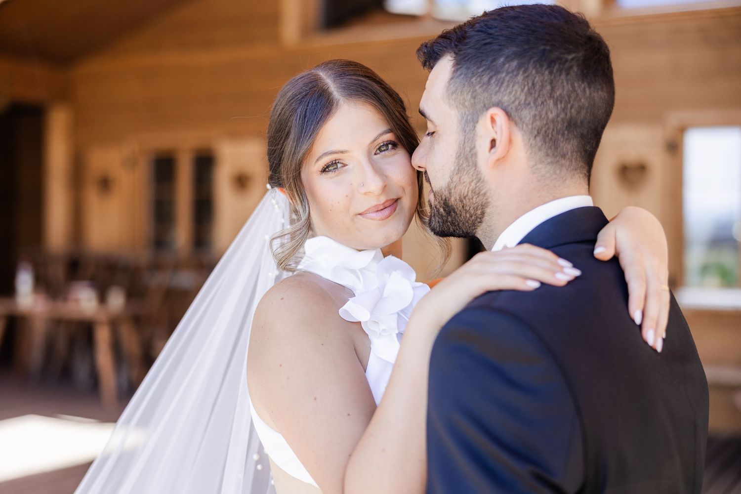 Bride in white gown and veil embraces groom in navy suit during romantic outdoor wedding portrait.