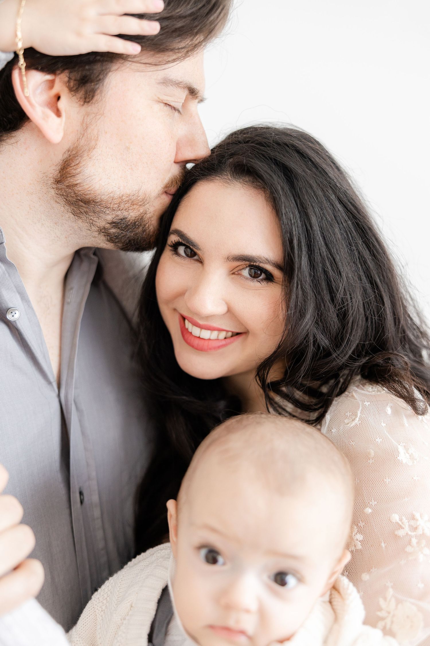 A loving family portrait shows parents cuddling their baby in a bright, intimate setting.
