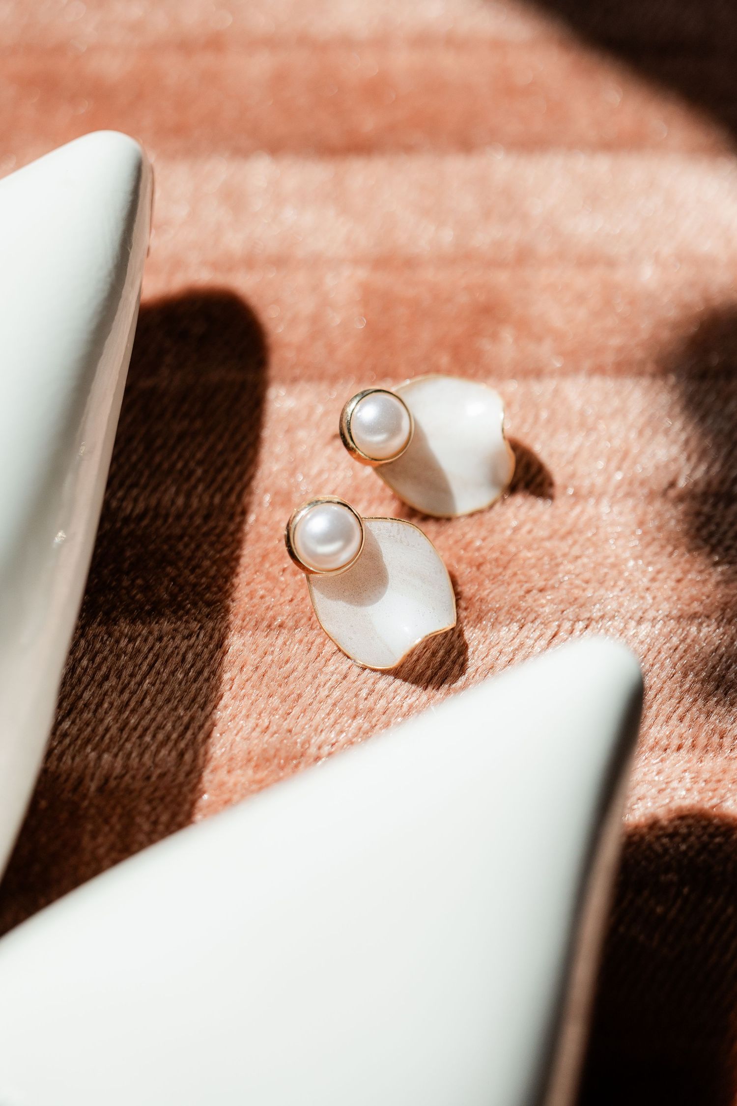 Gold and pearl drop earrings with white shell accents on a brown plaid fabric surface.