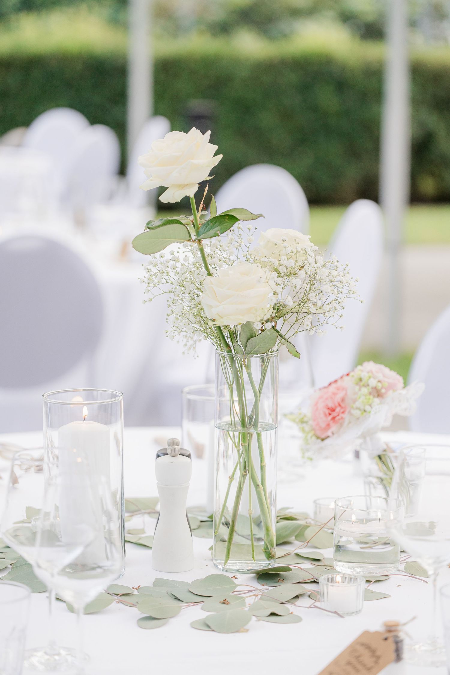 Elegant wedding table settings with delicate white floral centerpieces in glass vases on crisp white tablecloths.
