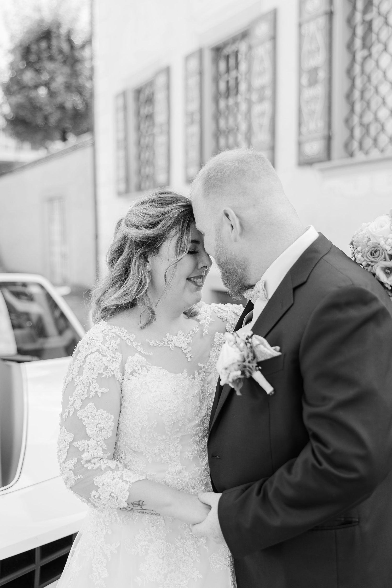 Black and white wedding photograph showing a tender moment between newlyweds in elegant formal attire.