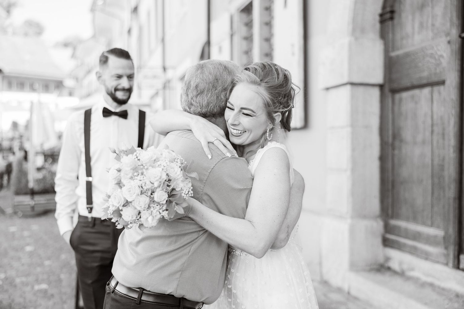 A joyful wedding moment captured in black and white as the bride embraces a guest while holding a bouquet.