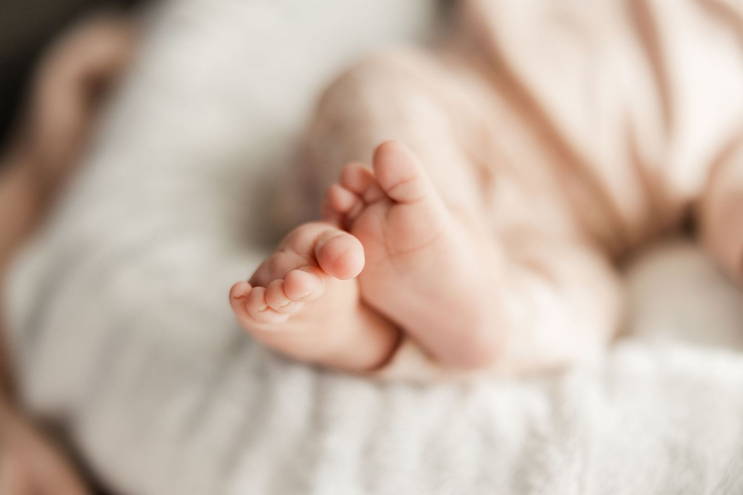 Close-up view of tiny newborn baby feet wrapped in soft white blanket showing delicate toes and skin texture.