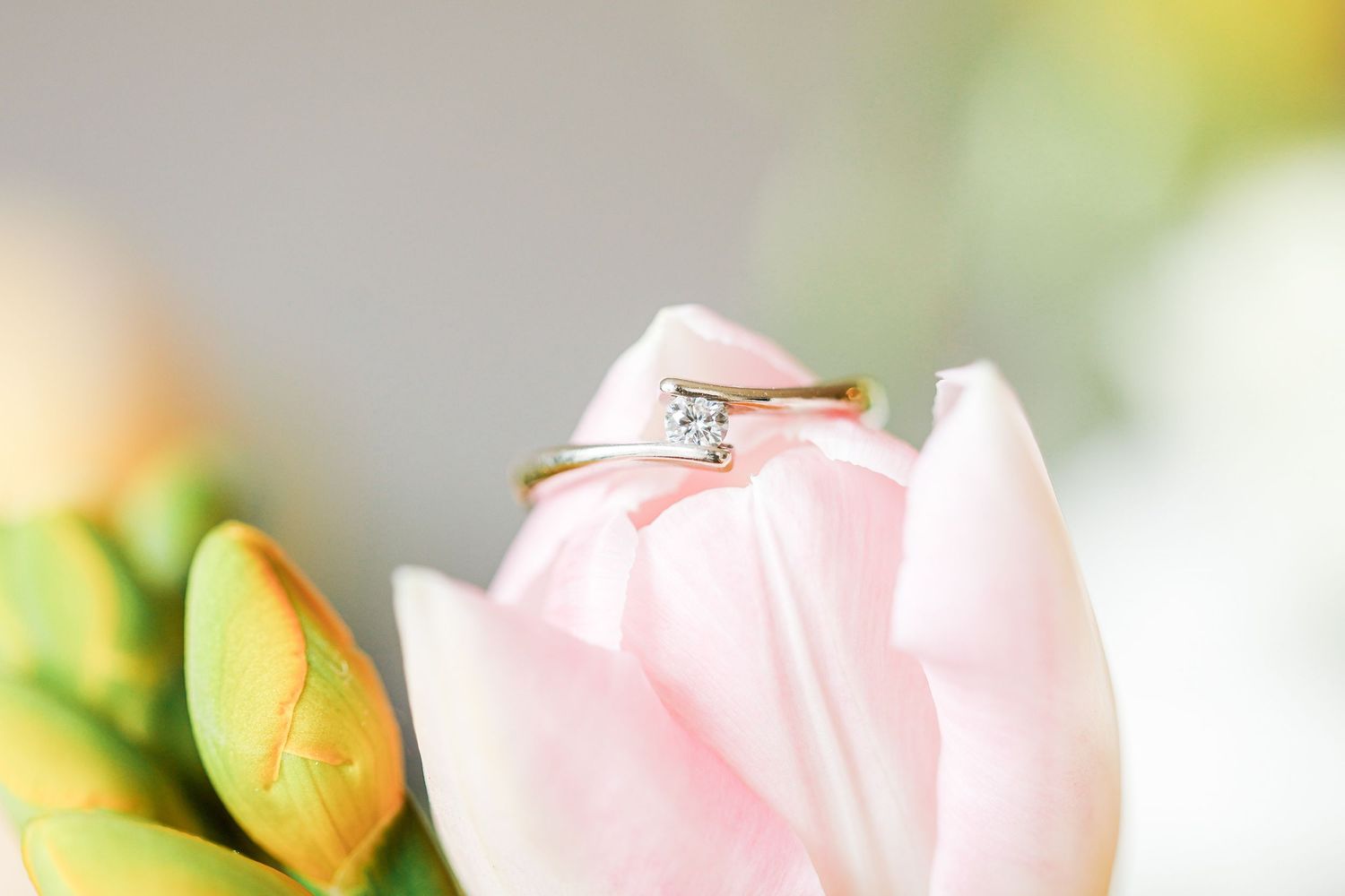 Gold solitaire diamond engagement ring resting inside a delicate pink tulip flower with soft bokeh background.