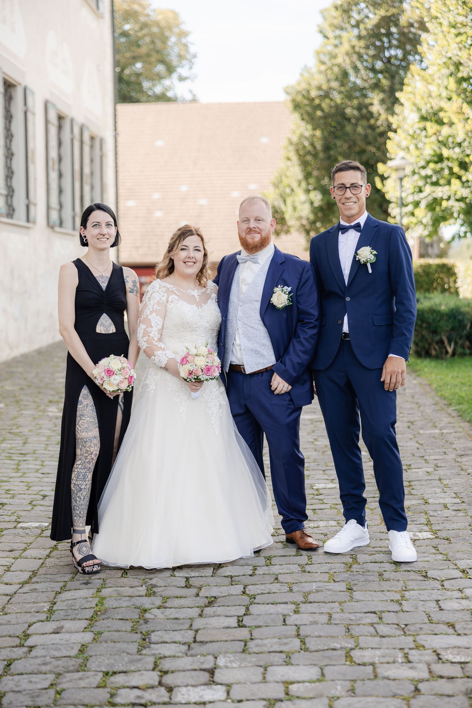 Wedding party in navy blue suits and white dresses pose together on cobblestone path outdoors.