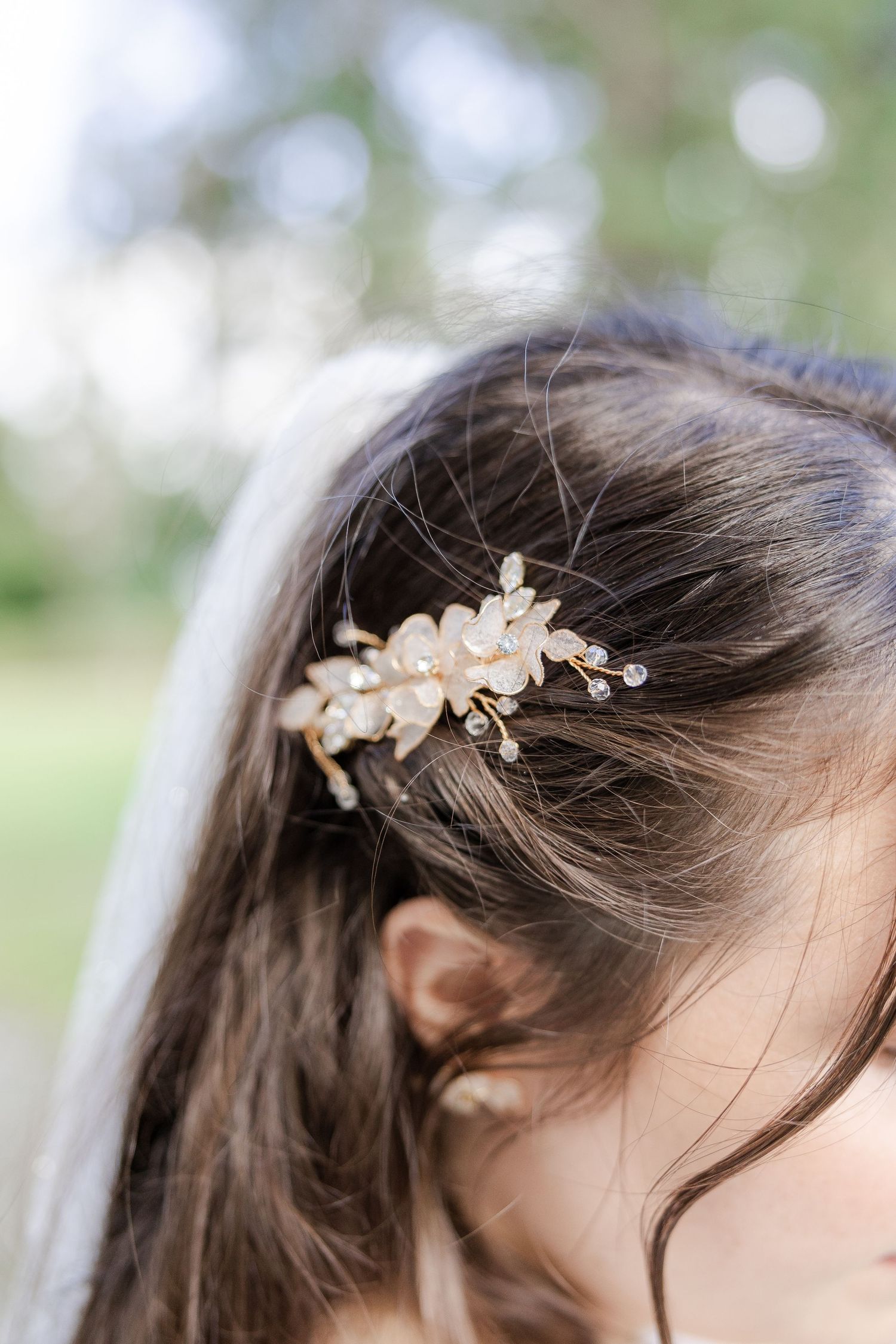 A delicate gold leaf hair accessory adorns dark hair with a soft blurred background.