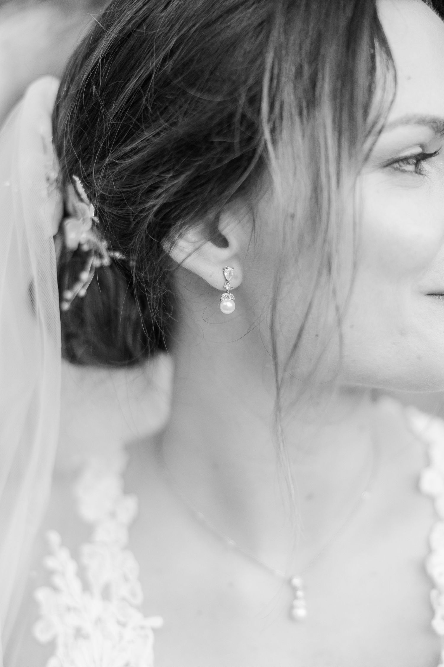 A black and white close-up portrait showing elegant drop earrings and delicate lace details of bridal attire.