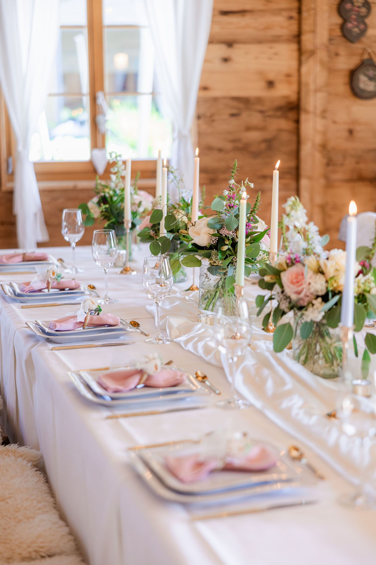 Elegant wedding reception table with pink napkins, floral centerpieces, candles, and crystal glasses on a white tablecloth.