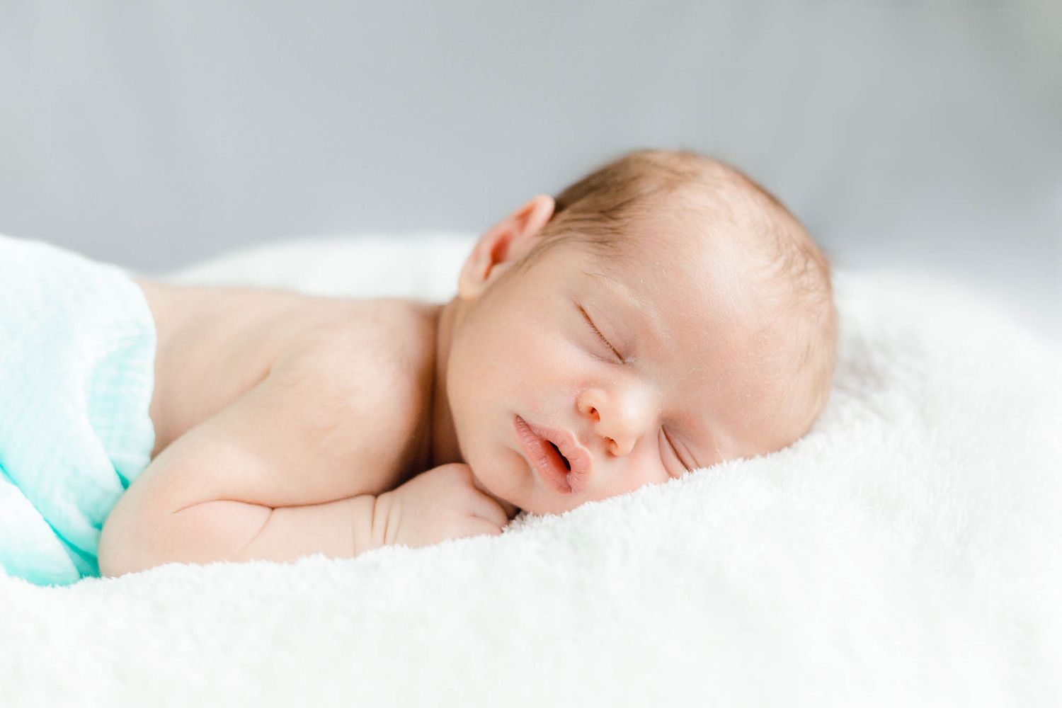 A peaceful sleeping newborn baby rests on soft white bedding with natural lighting.