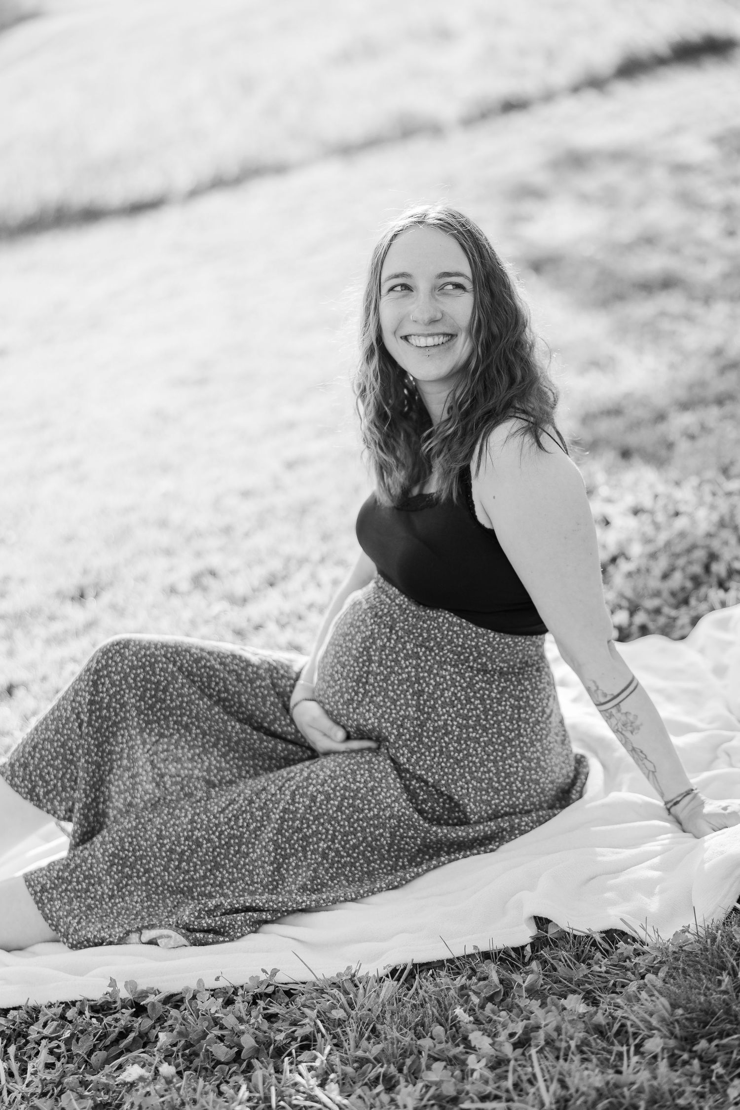 A series of black and white portraits showing someone reclining on grass wearing a patterned dress in natural light.