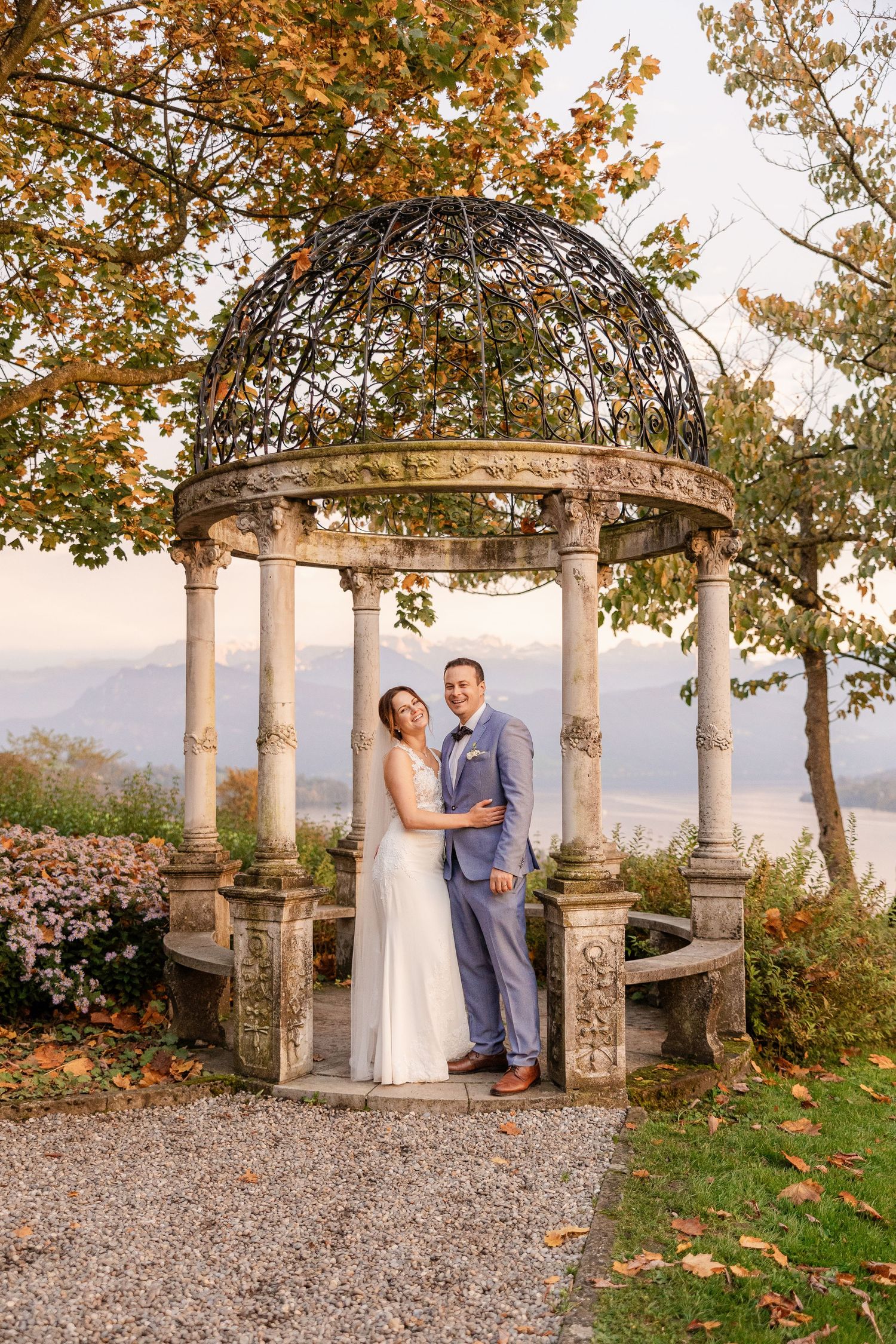 Stone gazebo surrounded by autumn foliage at golden hour creates romantic setting for a wedding moment.