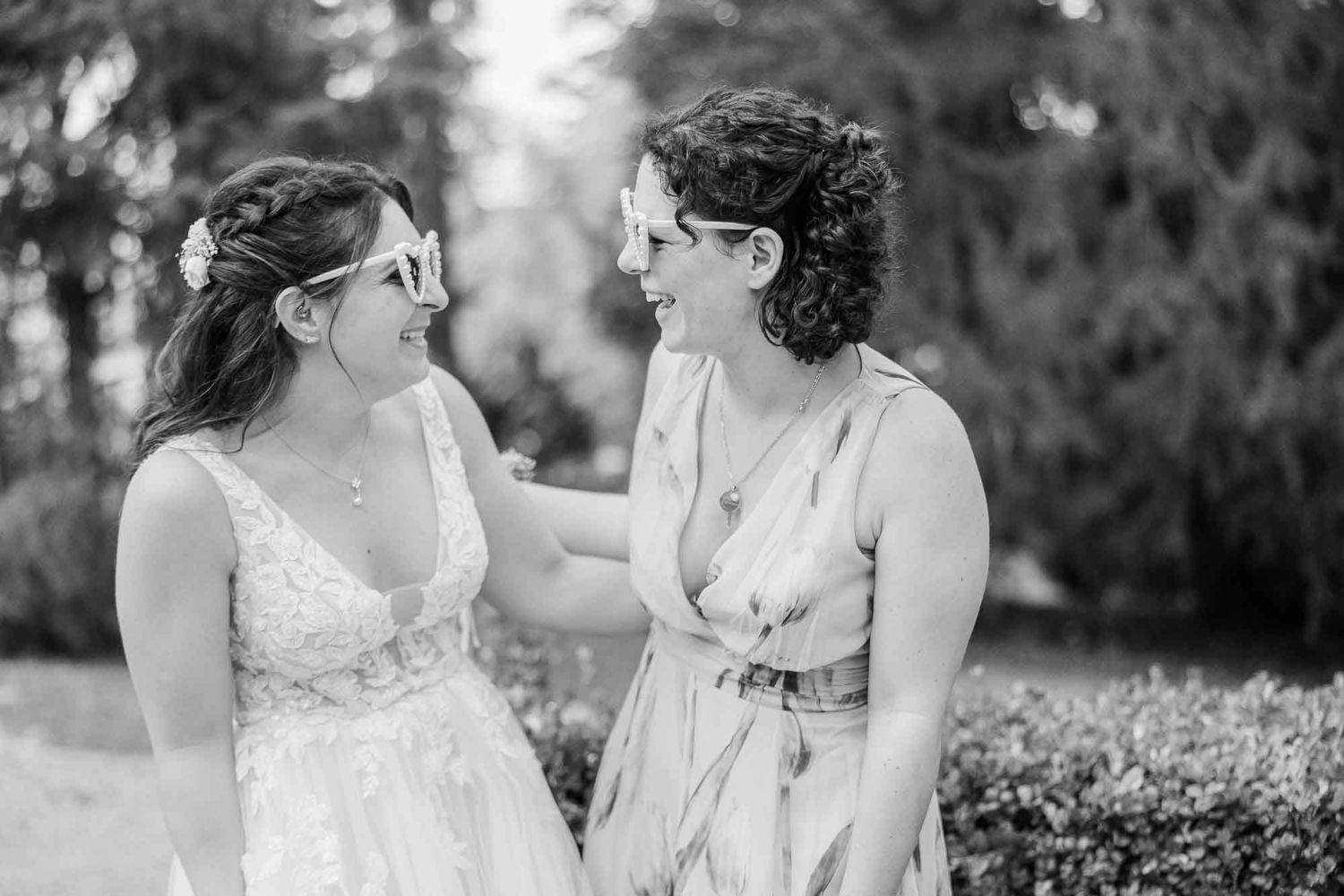 Two brides share a joyful moment outdoors in black and white wedding photo.