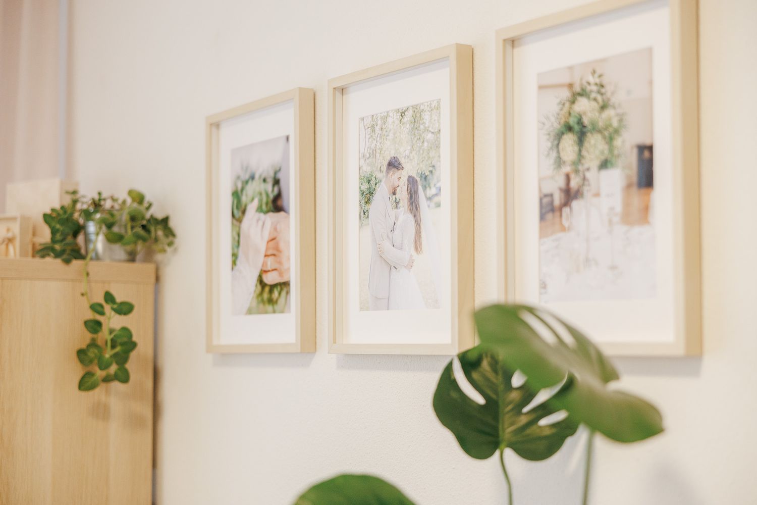 Gallery wall display with framed artwork and decorative monstera leaves in a light beige interior space.